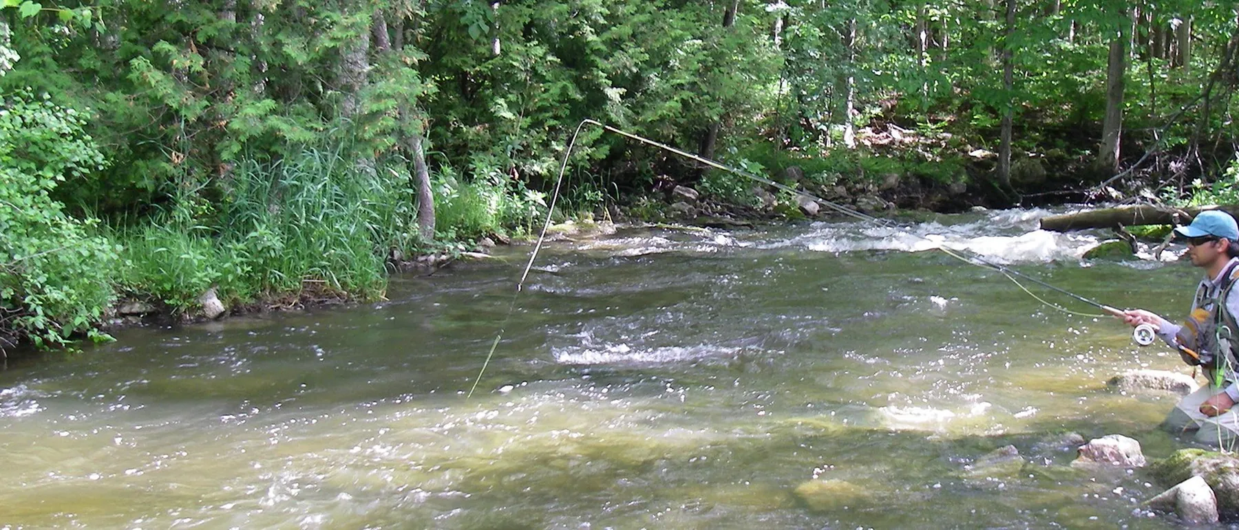 A wide view of a Southern Ontario river with an angler working a run