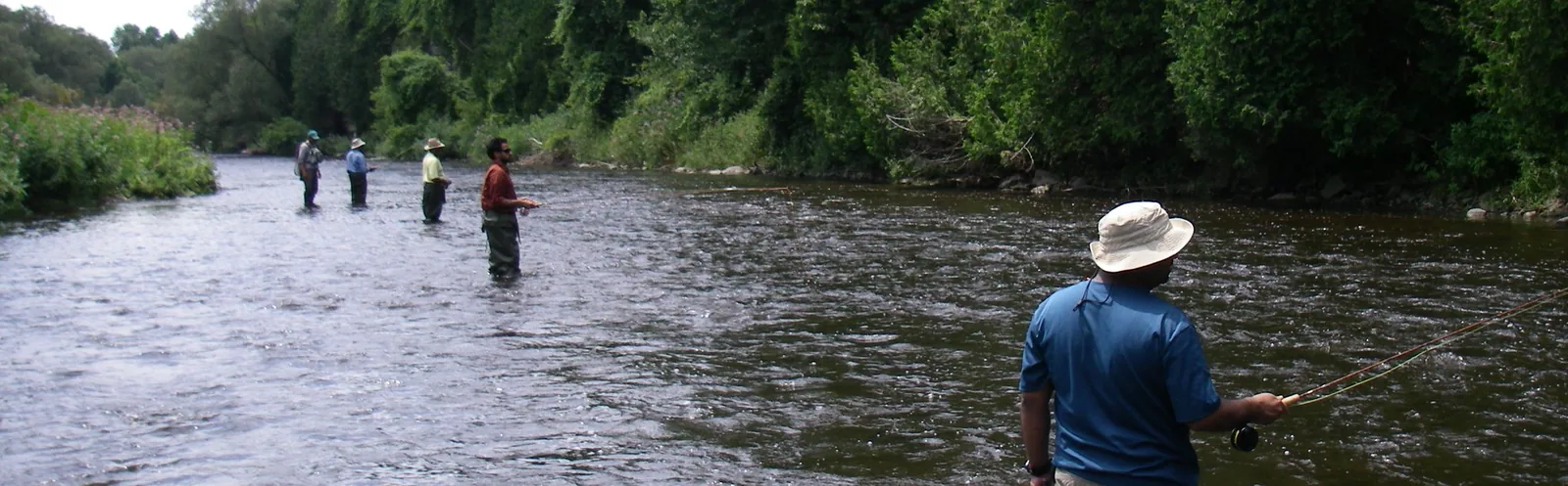 A group of anglers spread across a summer river casting during an on-the-water session
